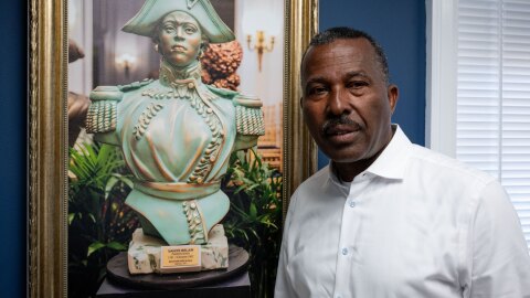 Norwalk Realtor Guy Bocicaut stands next to a photo featuring a bust of Haitian revolutionary leader Sanité Bélair at his offices in Norwalk on July 15, 2025. Bocicaut has called for a series of boycotts by immigrants and is seeking support from immigrant rights advocates.