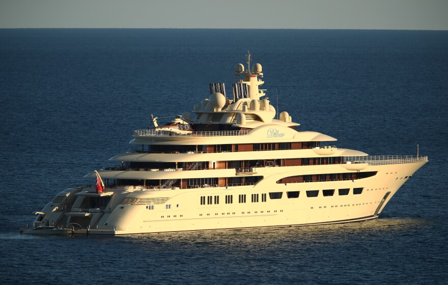 A massive yacht sails away from the camera in blue waters.