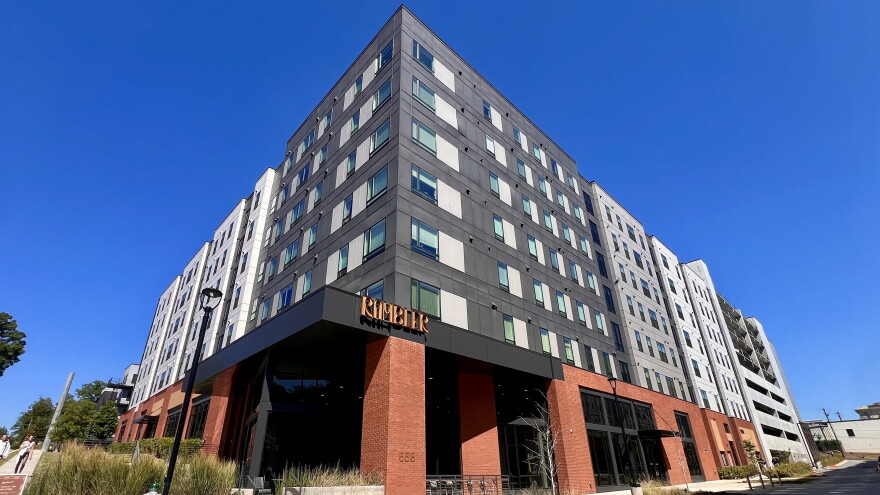 A 8-story grey and brick apartment building on a corner.