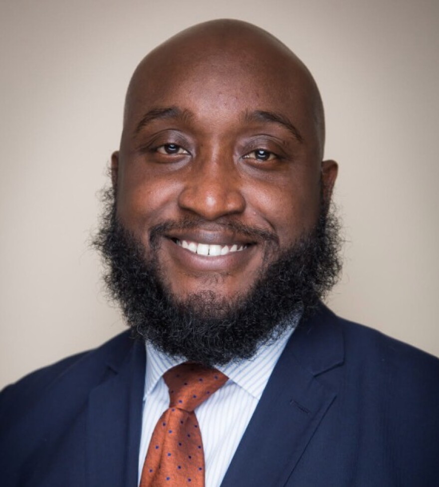 A portrait photo of a bald man with a full beard wearing a suit and tie. 