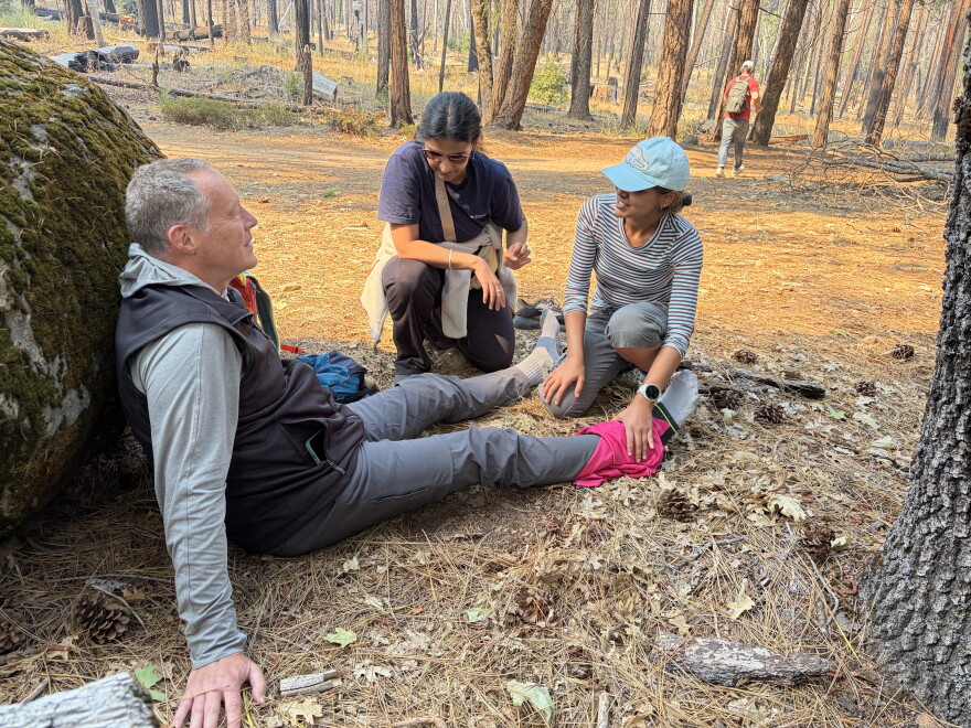 Two medical students help a hiker who hurt his ankle—first by assessing the severity, then by applying a makeshift ankle wrap with an extra shirt.