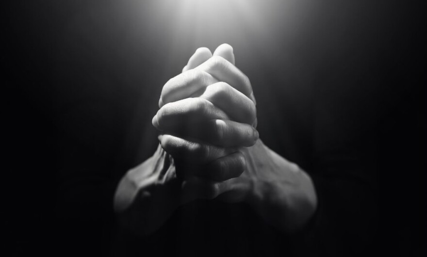 Hands clasped together in prayer against dark background with light beaming down