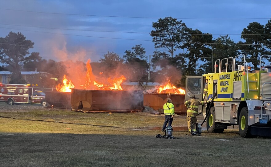 A training fire inside roll-off dumpsters gets bigger as dusk starts to fall during an emergency drill at Cape Cod Gateway Airport in Hyannis, Sept. 26, 2024.