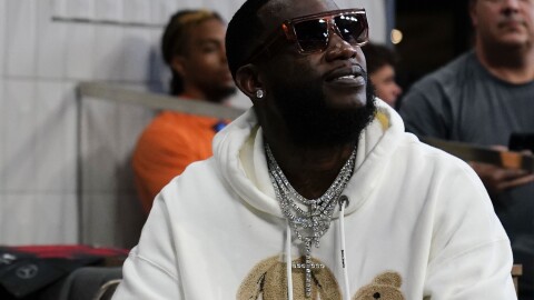 A smiling man in a white hoodie, a diamond necklace and sunglasses