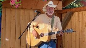 A white man in a cowoby hat playing an acoustic guitar