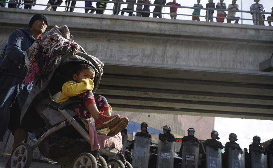 A migrant man pushes a child in a baby stroller past a cordon of riot police as he joins a small group of migrants trying to cross the border together at the Chaparral border crossing in Tijuana, Mexico, Thursday, Nov. 22, 2018. 