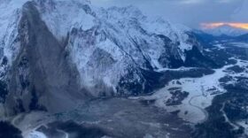On a cloudy day, a massive landslide is visible in the mountain