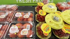 Interior photo of a grocery store section that shows a shelf with large and  small tomatoes packed in plastic containers.