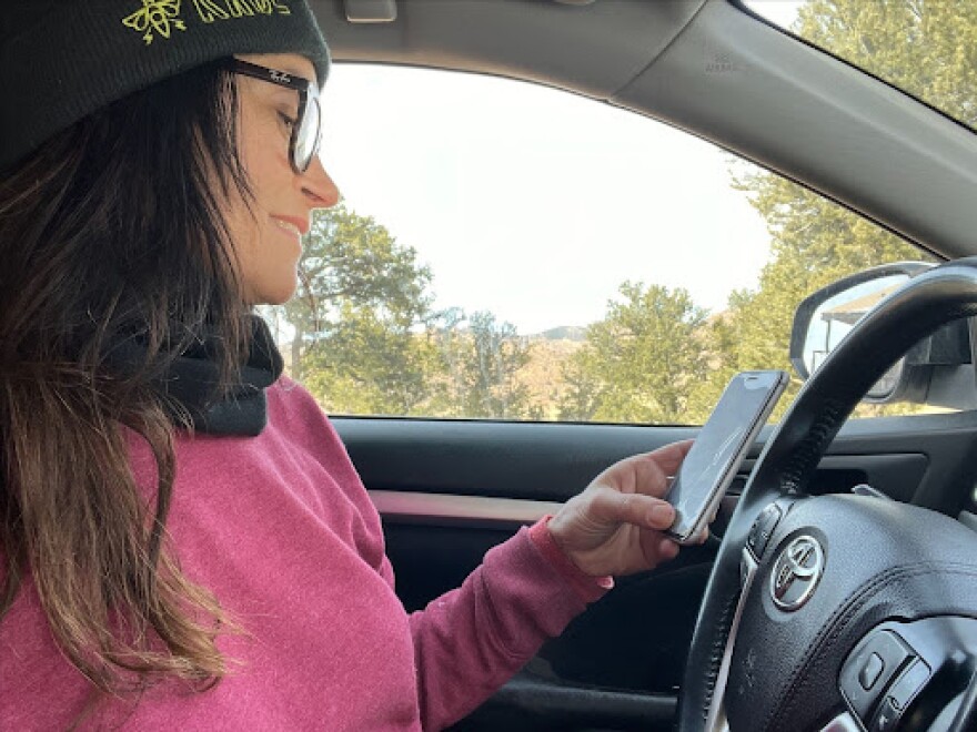 A driver checks messages on her phone while in her vehicle. Beginning January 1, 2025, this will be illegal.