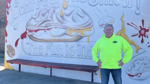 A man stands in front of a wall painted with hamburgers and the slogan "Don't Fear the Smell! The Fun is inside!!"