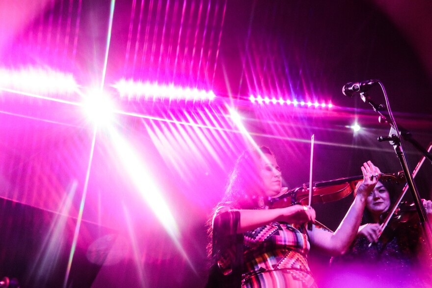 Two violinists perform, illuminated by starry lights.