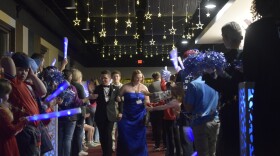 two people walk down a red carpet with two vertical parallel lines of people cheering