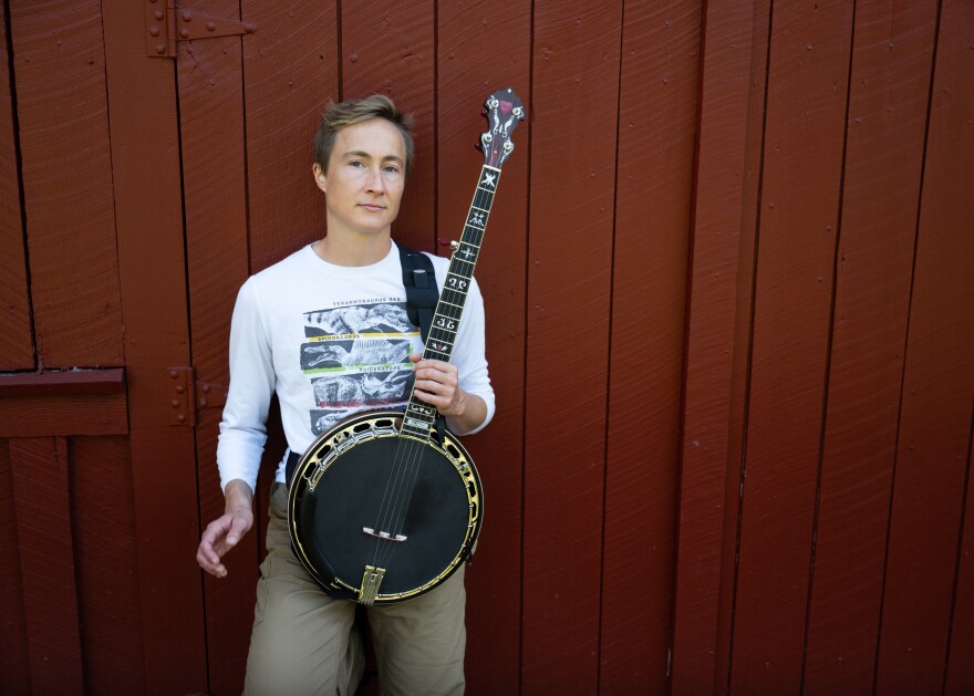 a man standing in front of a red exterior wall holding a black and gold banjo