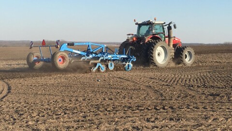 A red tractor hauls a blue, metal-framed planter across a brown, barren field that's criss-crossed with tire marks. 