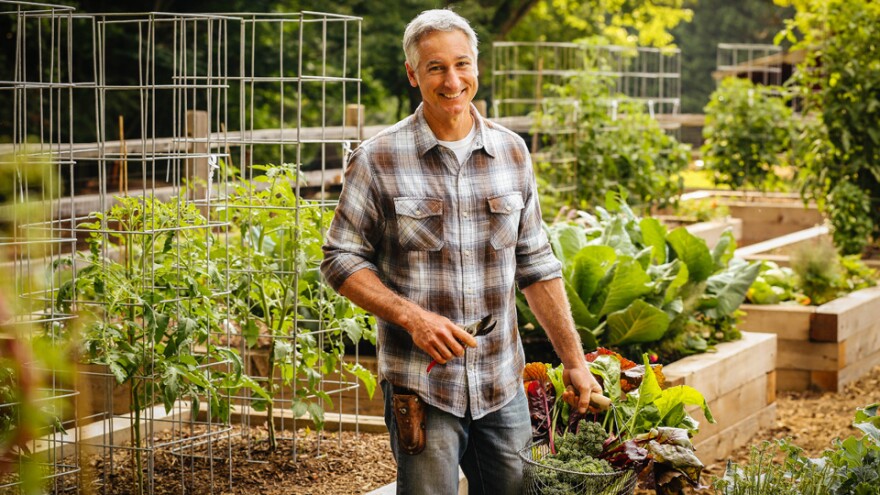Photo of a man standing in a garden with a basket full of crops