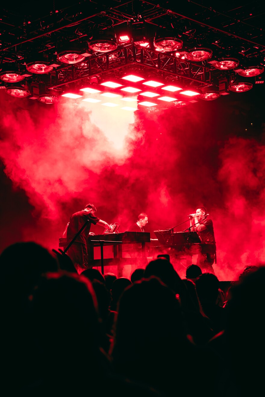 Three people performing music live with red lights 
