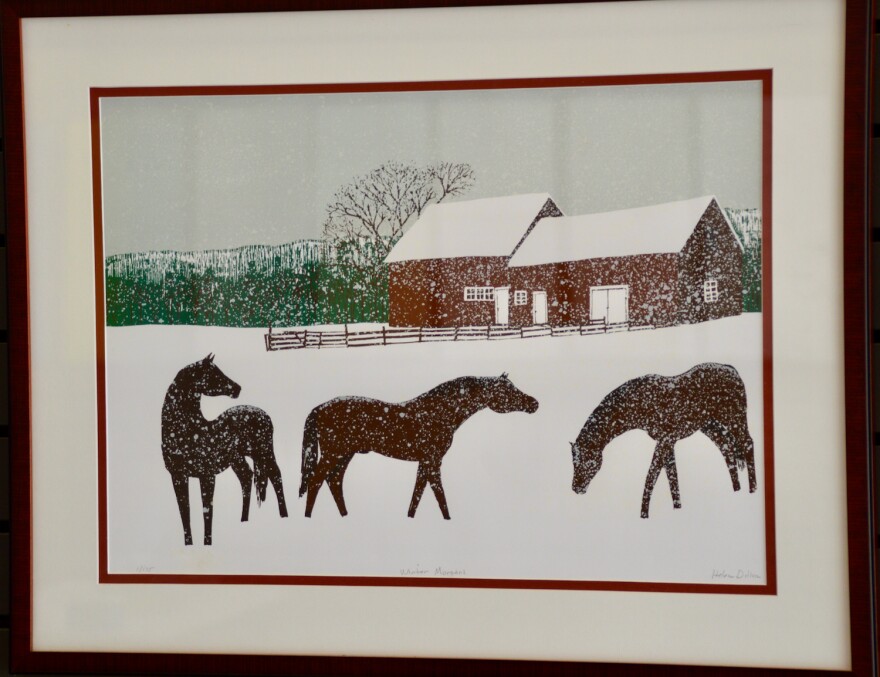 Framed printed image of three brown horses gathering in snowstorm in front of red barn.