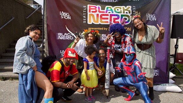 People in colorful costumes pose in front of a banner.