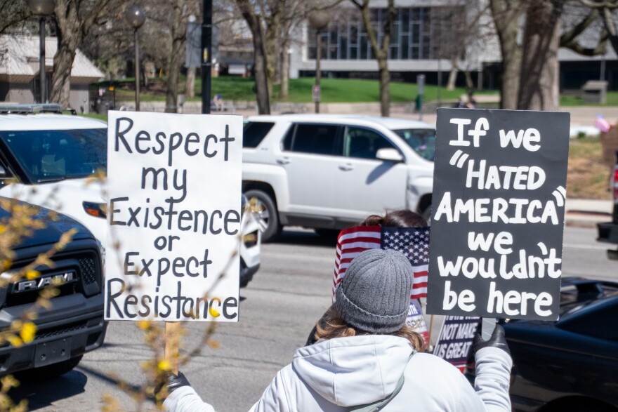 A protester holds two signs up to traffic on South Calhoun Street in downtown Fort Wayne on Saturday. Protesters stretched down both sides of the street, from the intersection of East Berry Street down past the Rousseau Center.