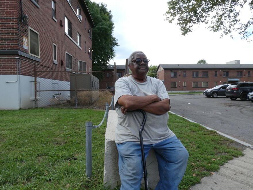 Wilson rests on a concrete roadblock outside of her Pioneer Homes apartment in Syracuse. Unable to get hearing aids, Wilson has to use a cane keep her balance.