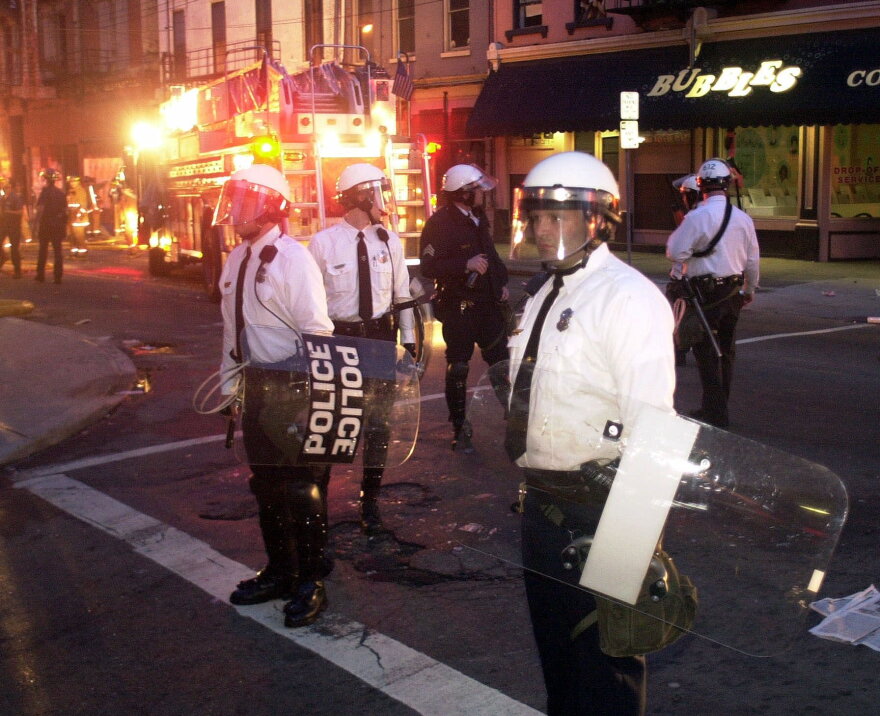 Cincinnati Police in riot gear stand gaurd as firefighters put out a fire started in Over-the-Rhine, Tuesday, April 10, 2001, following protests over the fatal police shooting of an unarmed black man turned violent.