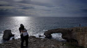 A couple hug each other as they stand next to the natural rock bridge that is named "Love Bridge", in Ayia Napa, on the southeast Mediterranean island of Cyprus. (Petros Karadjias/AP)