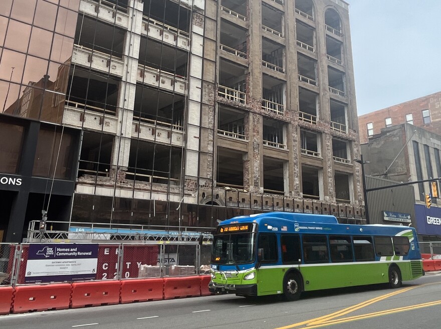 An RTS bus travels down East Main Street in downtown Rochester on May 22, 2026, passing the Gateway and Cornwall buildings where crews are stripping away glass panels that have covered the structures for decades. The work is part of the 129-unit Gateway Apartments redevelopment project.