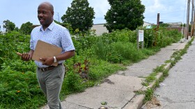 A man walks along a sidewalk that is somewhat uneven and there is grass growing between the cracks.