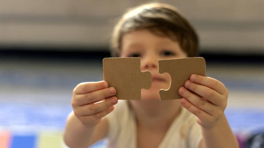 Puzzles in the hands of a child on colorful background.Boy at home playing with puzzles.Cute little child connecting a jigsaw pieces.Portrait of toddler holding jigsaw puzzle block,looking at camera.