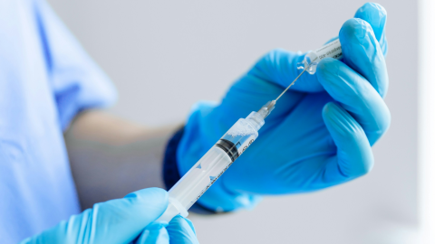 A health practictioner, mostly off-camera, fills a syringe with clear liquid.