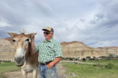 A man and a mule stand in a pasture in front of a mountain.