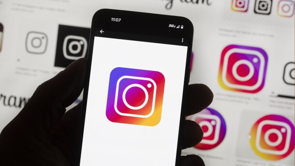 A backlit hand holds a phone with the Instagram logo on it.
