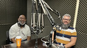 Two men sit smiling at a table in a recording studio.
