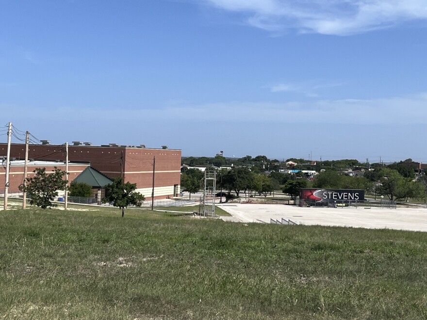 A brick school building with a band trailer in the foreground, with a business district behind it.