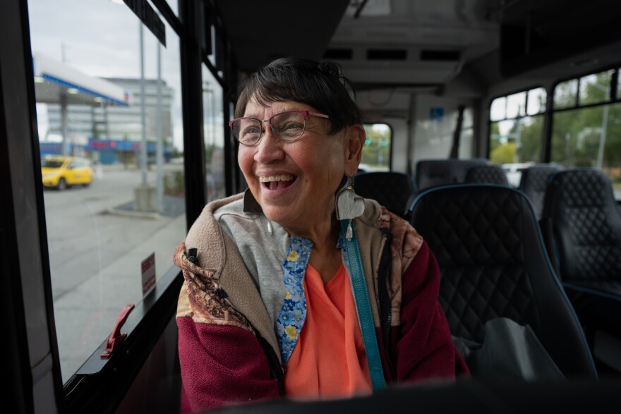 A woman with short hair and glasses rides a bus.
