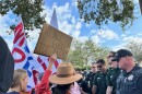 Protesters hold up signs speaking out against immigration enforcement as local officers tell them to move off the grass