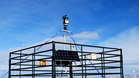 Air quality monitoring device powered by a solar panel and surrounded by a fence