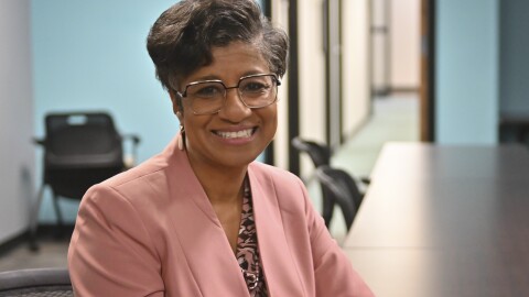 A woman sits inside a meeting space looking at the camera and smiling.
