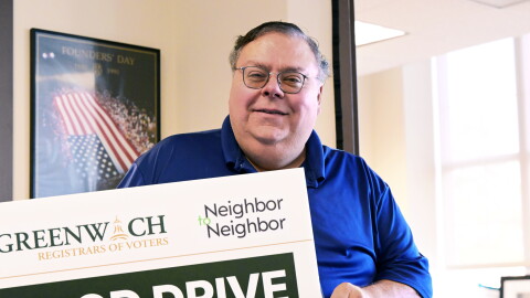 Republican Registrar of Voters Fred DeCaro III holds up a sign promoting a food drive by Neighbor to Neighbor, a local nonprofit that also has a donation bin at Greenwich Town Hall during early voting on October 20th, 2026. DeCaro said he's already received a full bin of donations since the drive commenced on Monday.