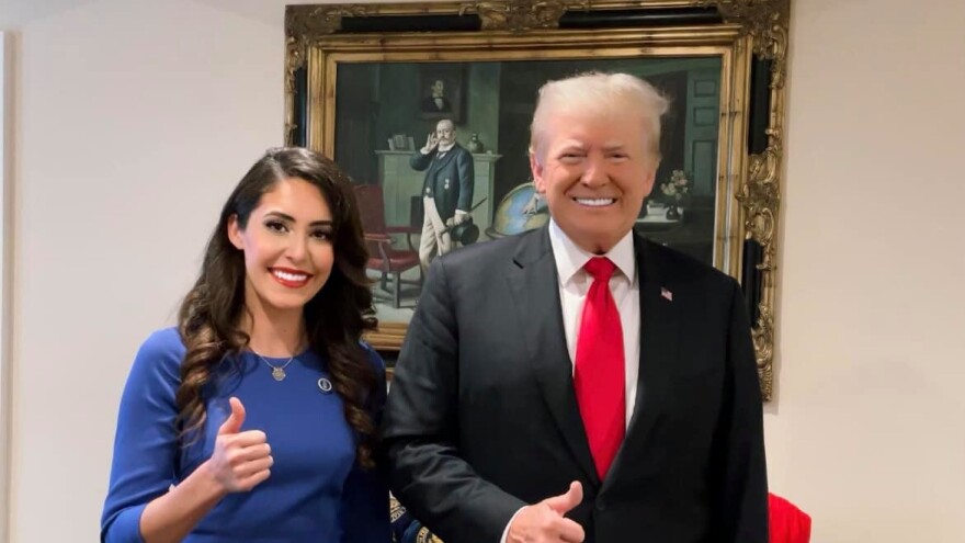 Woman in blue dress standing next to man in suit and red tie. Both are smiling and giving a thumbs up gesture.