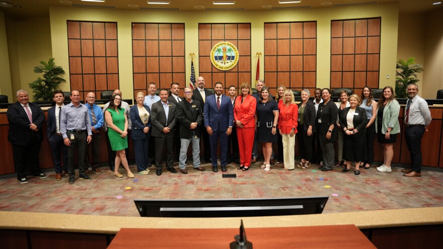 Denise Carlin (center, in red) addressed the media about Lee schools budget cuts on May 1, surrounded by administrators and other officials from the school district as well as Florida Commissioner of Education Anastasios Kamoutsas (at Carlin's right).