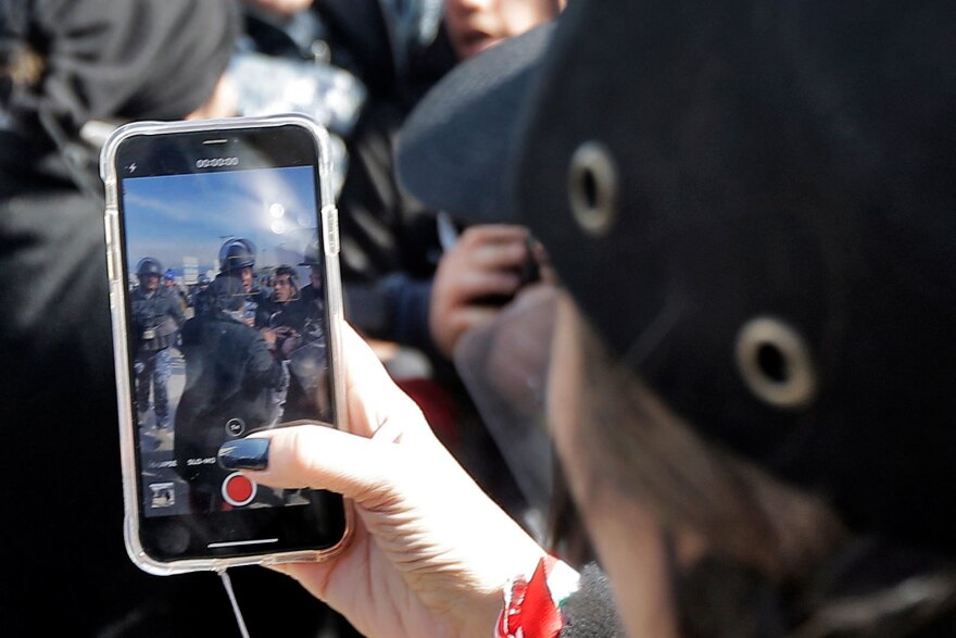A woman films with her phone as Lebanese security forces detain an anti-government protester during clashes in a demonstration in Beirut in January.