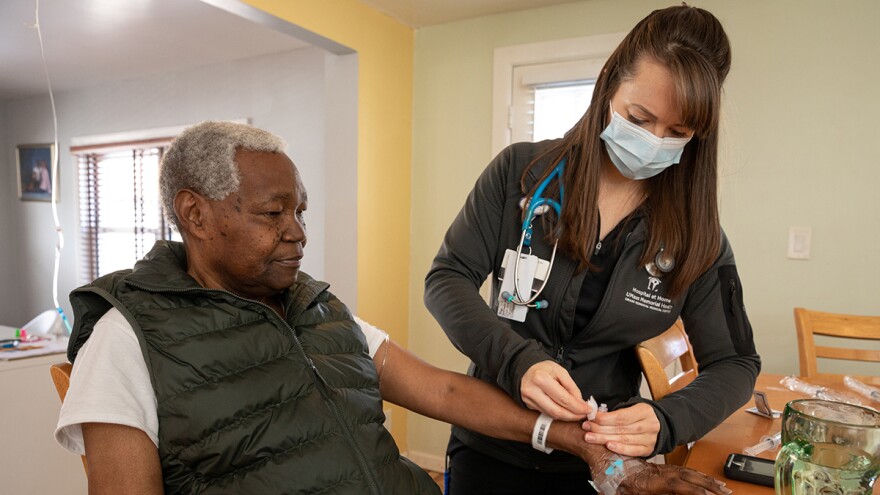 A patient sits in a chair awhile a nurse stands by his side.