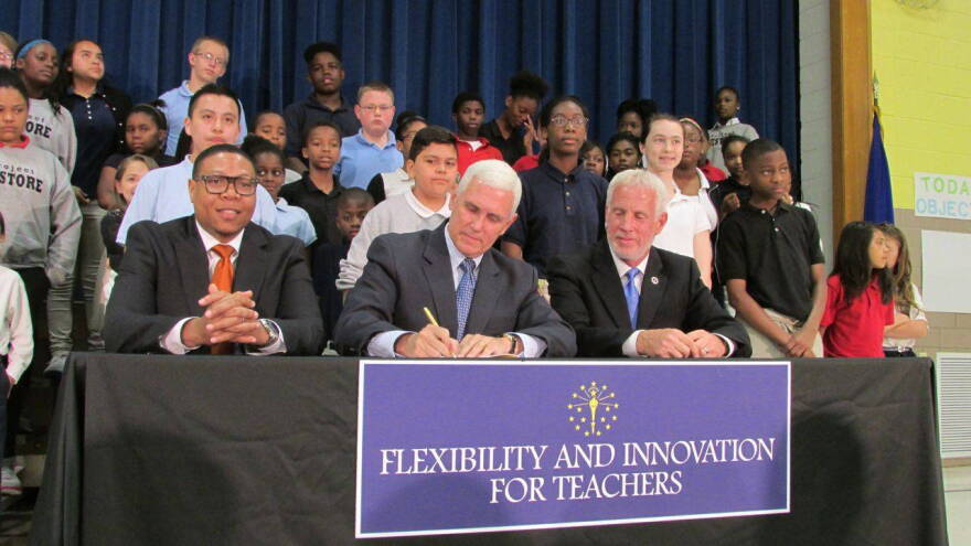 Pence signs House Bill 1009 while IPS Superintendent Lewis Ferebee (left) and Indiana House Education Committee Chairman Robert Behning, R-Indianapolis, and School 88 students look on.