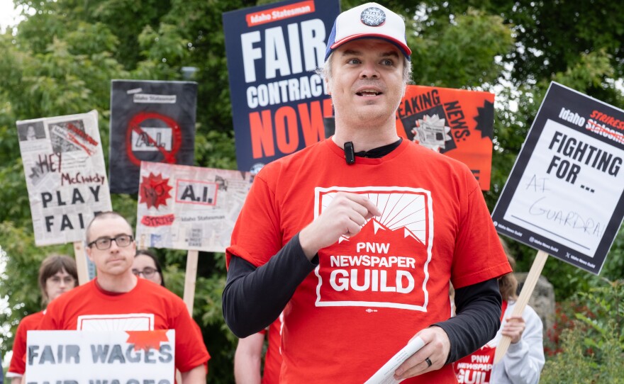 A group of newspaper reporters and photographers wearing red shirts hold picket signs as they strike for fair wages.