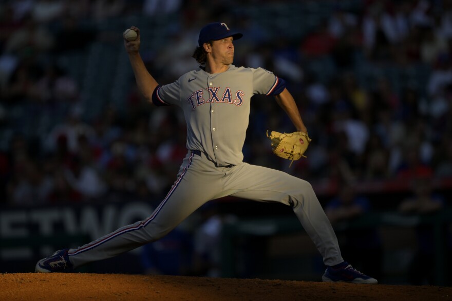 A baseball player in a gray uniform that says "Texas" pitches a baseball.