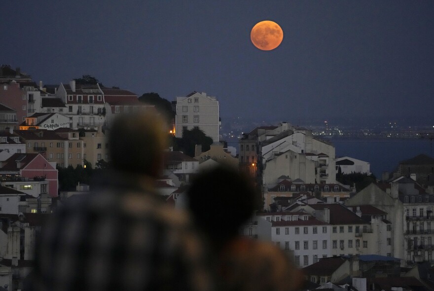 Lisbon, Portugal: Two people watch the supermoon rise from a viewpoint overlooking Lisbon and the Tagus river.