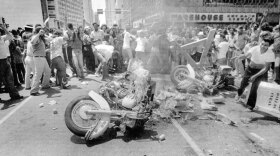 Crowd of demonstrators surrounding destroyed motorcycle on Dallas street.