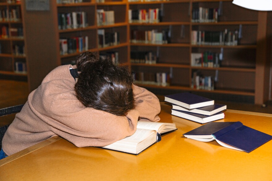 Tired female student brunette sleeping in university library at table with her head in her hands