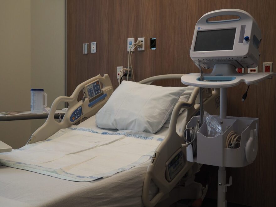 A hospital bed in a hospital room with a monitor to the right.